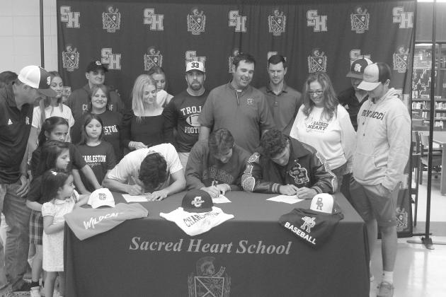 Karonika (left), Arnold (center), and Leger (right) sign their letters of intent while being surrounded by family members, coaches, and Sacred Heart Principal Dawn Shipp