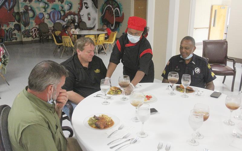 Erin Louis (standing) serves Paul Fontenot (second from left) the main course during the Flat Town Culinary Academy end of the year banquet. Also pictured are Philip  Buller (left) and Linton Fontenot (right). (Gazette photo by Tony Marks)
