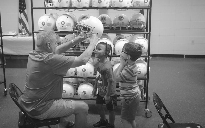 Ville Platte Lions Club member Dess Fontenot (seated) places a Flea Fly helmet on the head of Tevonn Charles (standing left) during the first day of registration. Also pictured (standing right) is Brayson Charles. (Gazette photo by Tony Marks)