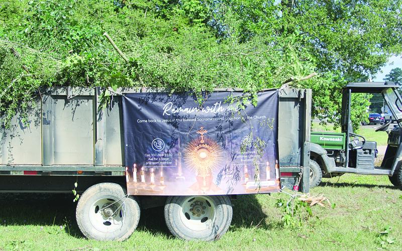 The “Remain With Me” banner hangs on a truck that is loaded with debris. “Remain With Me” is a three-year Eucharistic revival in the nation.