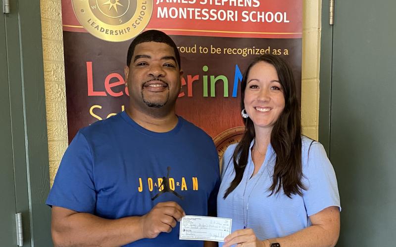 Chris Serie (left) presents a $500 donation to James Stephens Montessori Principal Melanie Bordelon for the school’s athletics program. (Photo courtesy of Melanie Bordelon)