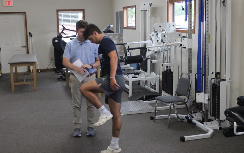 Clay Landreneau (left), a physical therapist at Healthworks Rehab, performs a physical examination on Sacred Heart’s Boyce Schexnider (right). (Gazette photo by Rhett Manuel)