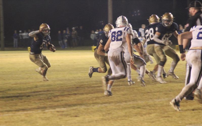 Sacred Heart quarterback Ethan Karonika (5) finds a running lane thanks to a block from his offensive line in the Trojans’ playoff win against disrtrict rival St. Edmund. (Gazette photo by Rhett Manuel)