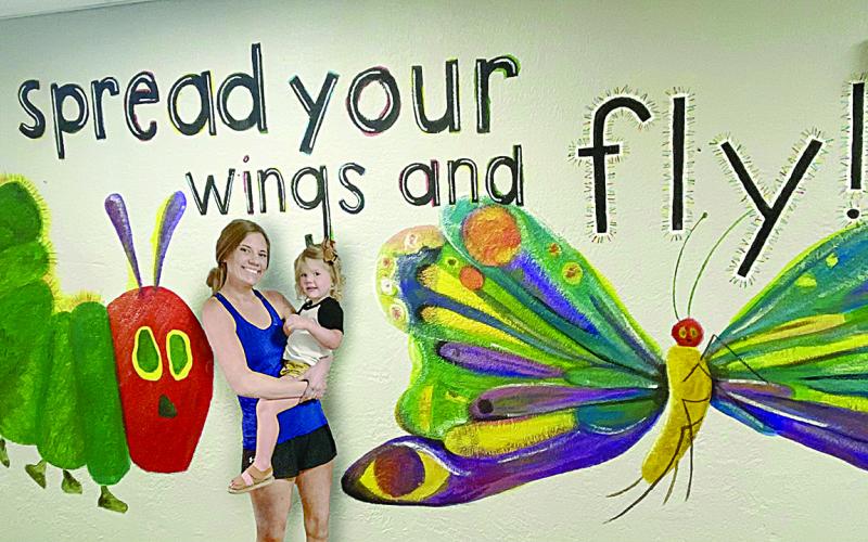 Lacey Vidrine is pictured with her two-year-old daughter, Cecille, in front of Very Hungry Caterpillar mural that she painted inside Vidrine Elementary. (Photo courtesy of Lacey Vidrine)