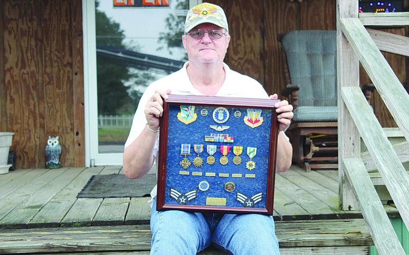 Michael Lee is pictured here sitting on the front porch of his business on Main Street in Ville Platte while holding the medals he received while serving in Vietnam. Among the awards he received is the Distinguished Flying Cross for a mission in Cambodia. (Gazette file photo)