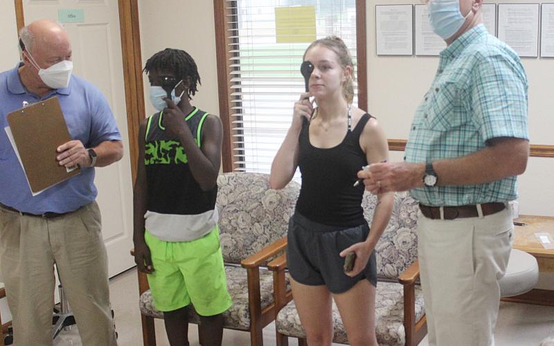 Dr. Hosea “Joey” Soileau (left) and local physical therapist Andy Poché (right) conduct vision screenings on two high school athletes at the athletic physicals held Thursday, July 29, at Healthworks Rehab in Ville Platte. (Gazette photo by Rhett Manuel)