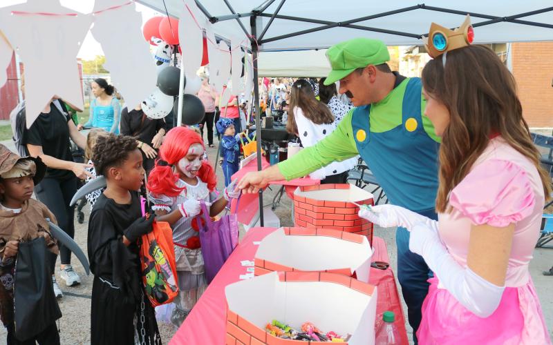 Ryan (center) and Jamie Vidrine (right), of Flat Town Farm Supply and Hardware, are dressed up as Luigi and Princess Peach as they pass out candy at the Rock the Block event held in Ville Platte on Thursday. (Gazette photo by Tony Marks)
