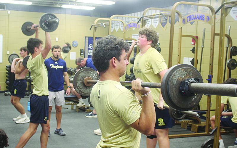 Sacred Heart head football coach Jacob Aguillard (center left) looks on as members of his team lift weights during summer workouts on Tuesday, June 9. (Gazette photo by Tony Marks)