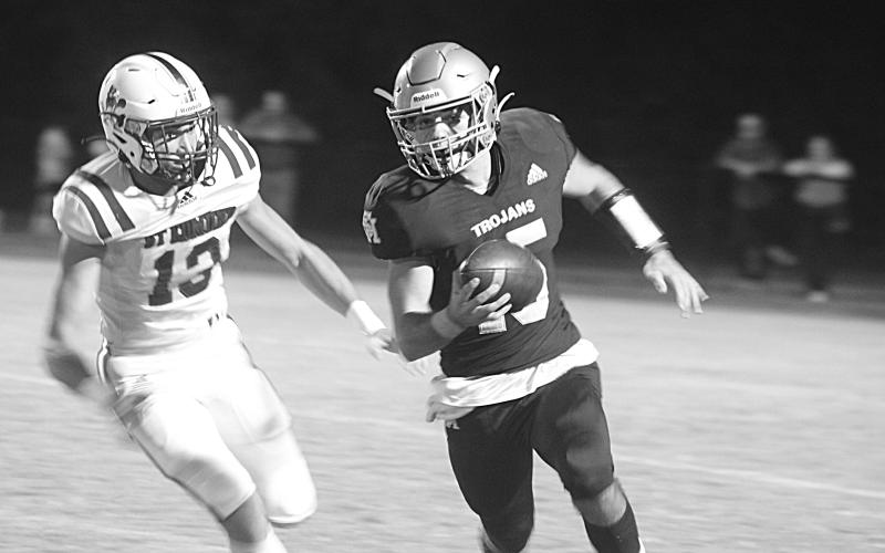 Trojan quarterback Wade Pitre (15) tries to avoid the grasp of a Blue Jay defender in Sacred Heart’s 21-14 home loss to St. Edmund last Friday night. (Gazette photo by Tony Marks)