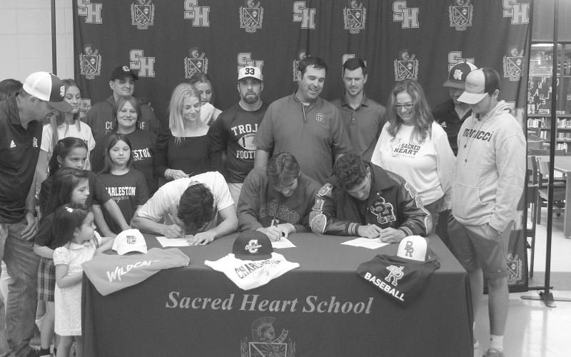 Karonika (left), Arnold (center), and Leger (right) sign their letters of intent while being surrounded by family members, coaches, and Sacred Heart Principal Dawn Shipp