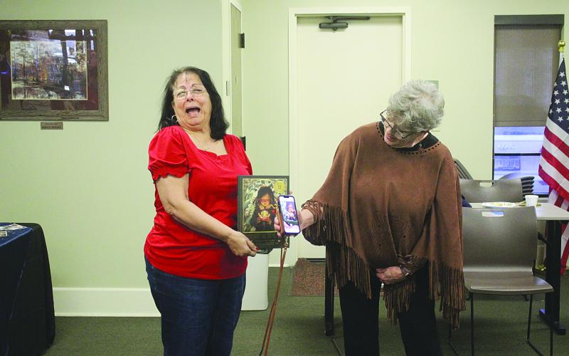 With the assistance of her cousin-in-law Joan Lemoine (left), Suzy Lemoine (right) shows off a book that blends artificial intelligence with the written word during her retirement ceremony held Wednesday, February 4. (Gazette photo by Tony Marks)