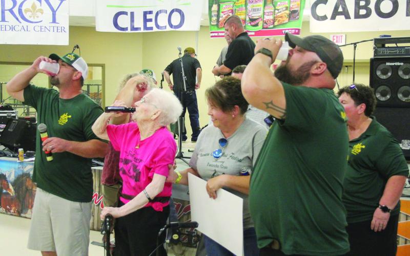 Carina “Tante Sue” Fontenot (center) takes a shot of Hot Damn out of her holster during the honoree presentation at the Mamou Cajun Music Festival. Among those also pictured are President TJ Landreneau (left) and Vice President Kade Verrette (right). (Gazette photo by Tony Marks)