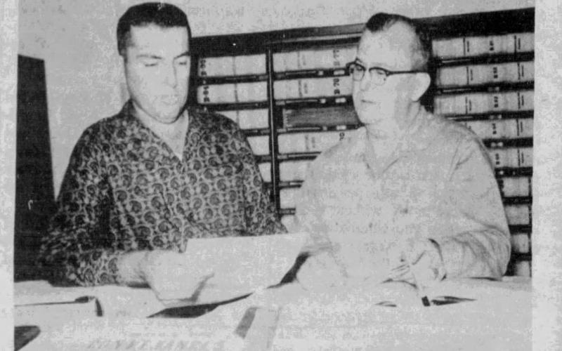 Clerk of Court Walter Lee and Deputy Louis Demoruelle look over legal documents by which president-elect John F. Kennedy transferred mineral holdings in Evangeline Parish to Janet DeRosiers, said to be the hostess-secretary of his personal plane. The mineral rights, acquired in 1951, are on property near Basile and will soon be expiring, unless production is begun within the coming year. (J. Quinn photo and caption - Dec. 29, 1960, Ville Platte Gazette)