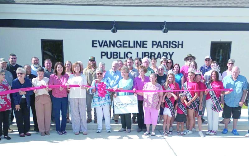 Local and parish library board members and employees, pastors, community leaders, library patrons, and Miss Basile royalty along with contractors who built the new Basile library branch building are gathered around Faye Langley, local representative on the Evangeline Library Board of Control, as she cuts the ceremonial ribbon at the library’s grand opening.