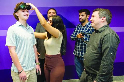 LSU psychology major Michael Cole Fontenot from Ville Platte, at left, does research on the human side of cyber. Part of a $600K DARPA project, Fontenot works to protect American soldiers by securing AR and VR technology from cyberattacks. Here, he gets a bit of assistance with the headgear from LSU computer science student Arushi Ghildiyal surrounded by teammates Professor Abe Baggili, Taha Gharaibeh and Assistant Professor Andrew Webb. (Photo by Elsa Hahne/LSU)