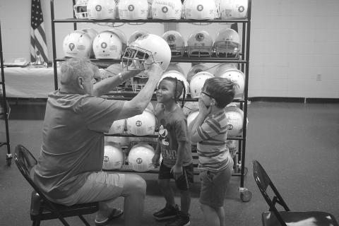 Ville Platte Lions Club member Dess Fontenot (seated) places a Flea Fly helmet on the head of Tevonn Charles (standing left) during the first day of registration. Also pictured (standing right) is Brayson Charles. (Gazette photo by Tony Marks)