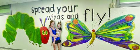 Lacey Vidrine is pictured with her two-year-old daughter, Cecille, in front of Very Hungry Caterpillar mural that she painted inside Vidrine Elementary. (Photo courtesy of Lacey Vidrine)