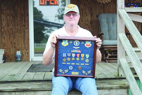 Michael Lee is pictured here sitting on the front porch of his business on Main Street in Ville Platte while holding the medals he received while serving in Vietnam. Among the awards he received is the Distinguished Flying Cross for a mission in Cambodia. (Gazette file photo)