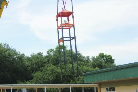 The new bell tower is pictured as Louisiana Crane hoists it over the covered walkway and places it in position at Pine Prairie High School on Tuesday, July 26. (Gazette photo by Tony Marks)