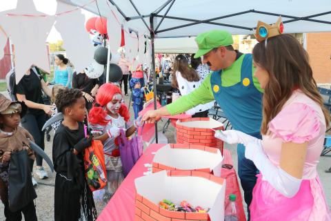 Ryan (center) and Jamie Vidrine (right), of Flat Town Farm Supply and Hardware, are dressed up as Luigi and Princess Peach as they pass out candy at the Rock the Block event held in Ville Platte on Thursday. (Gazette photo by Tony Marks)