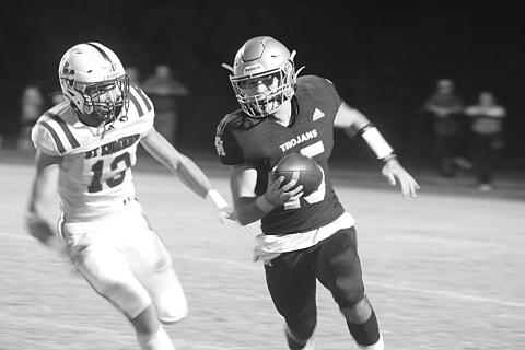 Trojan quarterback Wade Pitre (15) tries to avoid the grasp of a Blue Jay defender in Sacred Heart’s 21-14 home loss to St. Edmund last Friday night. (Gazette photo by Tony Marks)