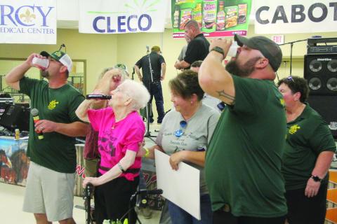 Carina “Taunt Sue” Vasseur (center) takes a shot of Hot Damn out of her holster during the honoree presentation at the Mamou Cajun Music Festival. Among those also pictured are President TJ Landreneau (left) and Vice President Kade Verrette (right). (Gazette photo by Tony Marks)