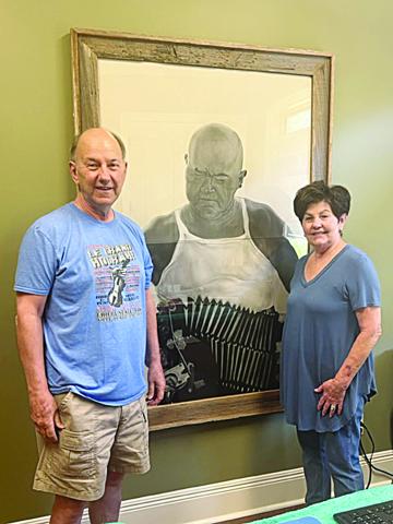 Gilbert “Winky” Aucoin (left) and his wife, Margaret “Chicken,” are pictured alongside an artist’s rendition of the late Cajun music performer Cyprien Landreneau, who is the father of Mrs. Aucoin. (Gazette photo by Tony Marks)