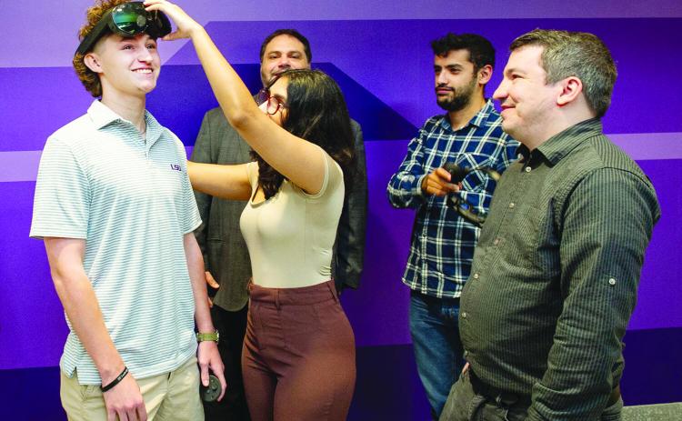 LSU psychology major Michael Cole Fontenot from Ville Platte, at left, does research on the human side of cyber. Part of a $600K DARPA project, Fontenot works to protect American soldiers by securing AR and VR technology from cyberattacks. Here, he gets a bit of assistance with the headgear from LSU computer science student Arushi Ghildiyal surrounded by teammates Professor Abe Baggili, Taha Gharaibeh and Assistant Professor Andrew Webb. (Photo by Elsa Hahne/LSU)