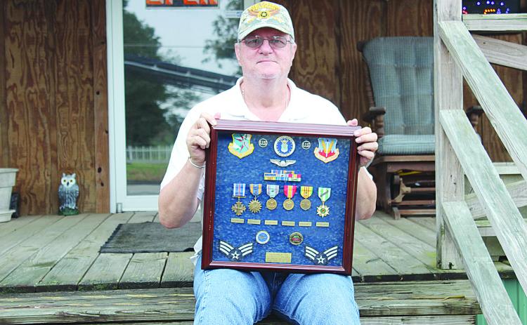 Michael Lee is pictured here sitting on the front porch of his business on Main Street in Ville Platte while holding the medals he received while serving in Vietnam. Among the awards he received is the Distinguished Flying Cross for a mission in Cambodia. (Gazette file photo)