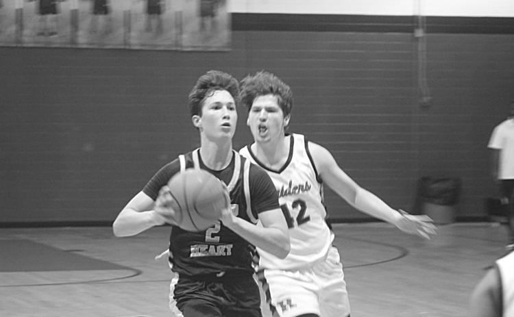 With Carter Guillory (42) nipping at his heels, Sacred Heart’s Ellis Chapman (2) looks to pass the basketball to a Trojan teammate. (Gazette photo by Tony Marks)