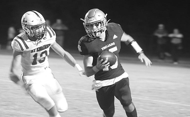 Trojan quarterback Wade Pitre (15) tries to avoid the grasp of a Blue Jay defender in Sacred Heart’s 21-14 home loss to St. Edmund last Friday night. (Gazette photo by Tony Marks)
